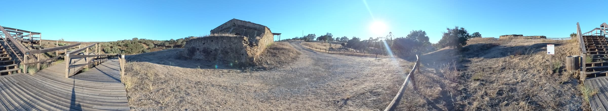 Panorâmica de 360° das Mesas do Castelinho ao fim da tarde: passadiço de madeira, muralha em ruína e o sol baixo a oeste